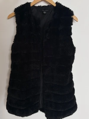 Svart pälsväst från Amisu - Snygg svart pälsväst från Amisu i mjukt fuskpälsmaterial. Västen är ärmlös, har en rak passform och stängs framtill. Perfekt att slänga över en hoodie eller tröja för en trendig lager-på-lager-look.