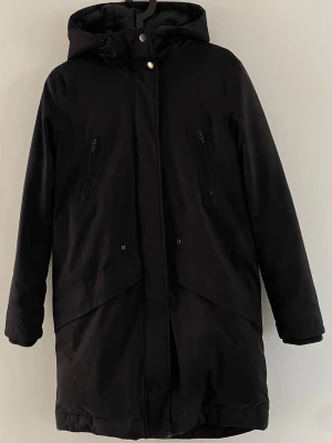 Samsoe samsoe - Svart dunjacka med dragkedjor - Svart lång dunjacka med två bröstfickor med dragkedja och två nedre fickor med dragkedja framtill. Även innerficka. Jackan är tillverkad av polyester, bomull, nylon och polyuretan, med mellanlager av 50% dun och 50% fjädrar. Perfekt för kalla dagar. Storlek framgår tyvärr inte men det är XS. Nytvättad. 