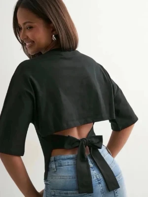 Svart topp med knyt i ryggen Xs - Trendig svart topp med halvlånga ärmar och snygg knytning i ryggen som ger en öppen rygg-effekt. Toppens passform är figurnära och den har en stilren, minimalistisk look. Perfekt att styla med jeans eller kjol. Strl Xs, använd max 3 gånger 💕