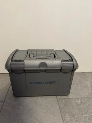 Grå förvaringslåda Hansbo Sport - Praktisk grå förvaringslåda från Hansbo Sport i tålig plast. Lådan har två mindre fack på locket och ett bärhandtag i mitten. Perfekt för att organisera småprylar eller hästtillbehör. Enkel att bära med sig tack vare handtaget.