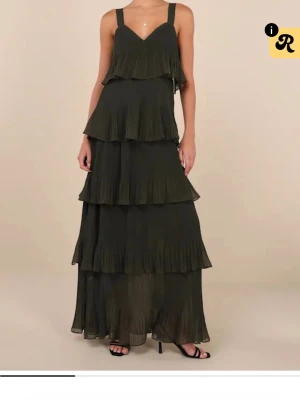 Svart långklänning med volanger - Snygg olivgrön balklänning med flera lager volanger och breda axelband. Klänningen har v-ringning och är tillverkad i ett lätt, plisserat material som ger ett luftigt intryck. Köpt från Lulu’s, aldrig använd utan bara testad💕