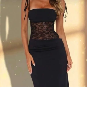 Svart långklänning med spetsdetaljer - Snygg svart långklänning med axelbandslös design och transparent spets i midjan. Klänningen har en figurnära passform och raka linjer, vilket ger en elegant siluett. Perfekt för dig som vill sticka ut med stilrena detaljer.