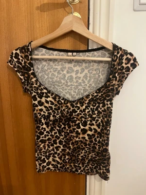 Leopardmönstrad topp från Nelly - Snygg leopardmönstrad topp från Nelly med korta ärmar och djup v-ringning. Toppens material är stretchigt och följsamt, perfekt för att skapa en trendig look. Färgerna går i beige, brunt och svart.