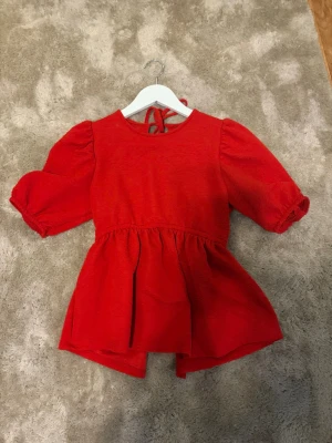 Röd puffärmad blus med knytband - Röd blus/topp med puffiga korta ärmar. Den har knytband både i nacken och baktill i midjan för en snygg passform. Endast använd en gång och därefter inte kommit till användning mer❣️