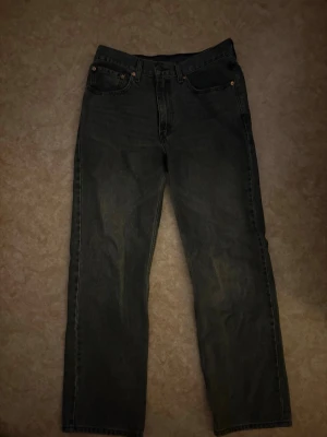 Levi's svarta/gråa raka jeans 565 - Säljer ett par svarta/gråa Levi's 565 jeans med rak passform och klassisk femficksdesign. Jeansen har en vintage look med slitningar och är tillverkade i kraftig denim. Perfekta för dig som gillar en avslappnad och tidlös stil.