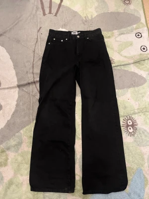 Svarta raka jeans från lager 157 - Säljer ett par svarta jeans från lager 157 med rak passform och klassisk femficksdesign. Jeansen har hög midja, bälteshällor och silverfärgade knappar. Materialet är kraftig denim i bomull. Perfekta för en avslappnad och trendig look.