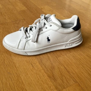 Vita sneakers från Polo Ralph Lauren - Snygga vita sneakers från Polo Ralph Lauren med klassisk logga på sidan och mörkblå detalj vid hälen. Strl 41, använt och fint skick.