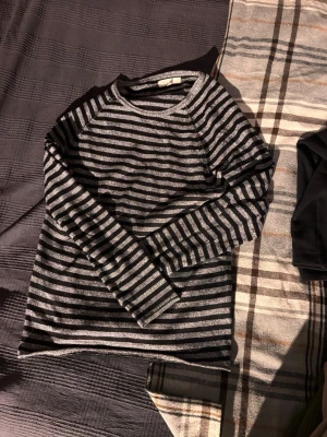 Randig stickad tröja från S.C.W. - Randig stickad tröja från S.C.W. i svart och grått. Tröjan har lång ärm och klassisk rund halsringning. Perfekt för dig som gillar en enkel men stilren look med lite edge.