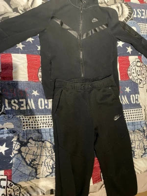 Svarta nike tech dress - Säljer ett par svarta mjukisbyxor från Nike med klassisk logga på vänster ben. Byxorna har dragsko i midjan och sidofickor. Tillverkade i mjukt och bekvämt material, perfekta för chill dagar eller träning. Matchar snyggt med en hoodie eller t-shirt.