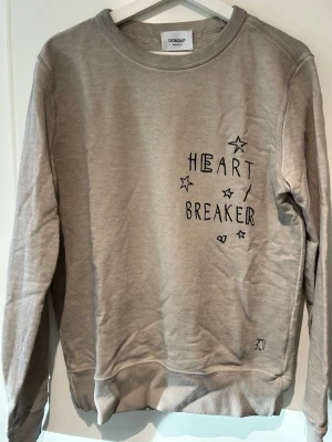 Grå sweatshirt Dondup Heartbreaker - Grå sweatshirt från Dondup med trycket 'Heartbreaker' och stjärnor på bröstet. Rund halsringning, ribbade muddar och avslappnad passform. Perfekt för en chill och trendig look.