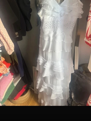 Vit maxiklänning med volanger - Säljer en lång, vit maxiklänning från True Decadence. Klänningen har flera lager volanger, spetsdetaljer upptill och v-ringning. Materialet är lätt och luftigt, perfekt för sommarens alla tillfällen. Romantisk och bohemisk stil med fina detaljer.