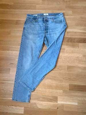 Ljusblå raka jeans från Jack & Jones - Säljer ett par ljusblå jeans från Jack & Jones med klassisk femficksmodell och raka ben. Jeansen har normal midja, bälteshällor och stängs med knapp och dragkedja. Perfekta för en avslappnad och trendig look.