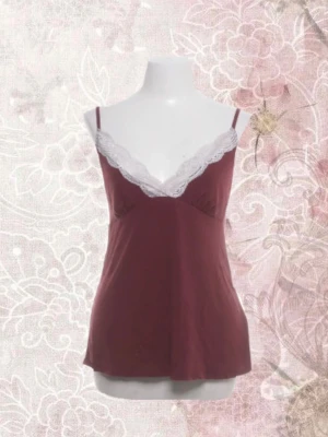 Babydoll linne med spetsdetalj  - Sött vinrött linne med smala axelband och vit spets längs v-ringningen. Mjuk och följsam passform, perfekt för lager-på-lager eller som den är. Spetsdetaljerna ger en romantisk touch. Materialet känns lätt och bekvämt mot huden.