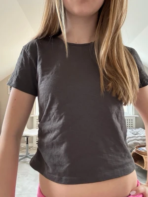 Mörkgrå croppad t-shirt med knyt - Snygg mörkgrå croppad t-shirt med korta ärmar och coola knyt-detaljer i sidan. Perfekt för dig som gillar en enkel men trendig stil. Gjord i mjuk bomull som känns skön mot huden.