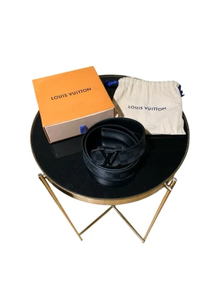 Svart Louis Vuitton bälte med LV-spänne - Snyggt svart bälte från Louis Vuitton med klassiskt LV-spänne i metall. Bältet har diskret rutigt mönster och levereras med originalförpackning och dustbag. Perfekt accessoar för att lyfta din outfit.