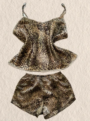 Leopardmönstrat satinset med spets - Snyggt tvådelat set i satin med leopardmönster. Setet består av ett linne med tunna axelband och spetskant samt matchande shorts med resår i midjan. Materialet är glansigt och mjukt, perfekt för en trendig look hemma.