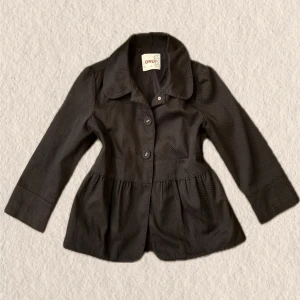 Svart kavajjacka från ONLY - Snygg svart kavajjacka från ONLY med markerad midja och två stora knappar framtill. Jackan har en klassisk krage, lång ärm och lätt utsvängd nederdel för en feminin siluett. Perfekt för att lyfta din outfit.