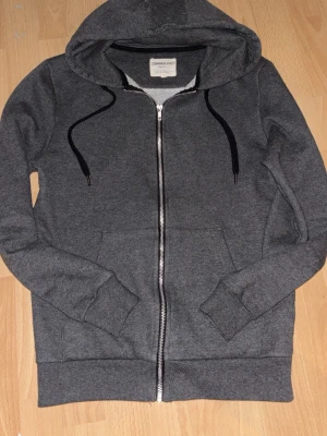 Mörkgrå zip hoodie med huva - Snygg💯 mörkgrå hoodie från Cedarwood state med dragkedja framtill, huva och svarta dragsnören. Tillverkad i mjukt sweatshirtmaterial och har två fickor framtill. Perfekt för en avslappnad och trendig stil.👌