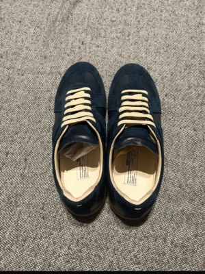 Maison margiela gats. Pris kan diskuteras  - Snygga mörkblå sneakers från Maison margiela med beige gummisula och matchande beige skosnören. Ovandelen är i en mix av mocka och slätt läder för en stilren look. Perfekta för dig som vill ha en klassisk men trendig sneaker.