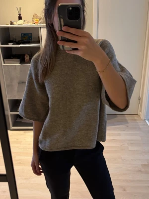 Grå/brun stickad tröja med vida ärmar - Säljer en grå/brun stickad tröja med breda, halvlånga ärmar och boxig passform. Tröjan har en enkel design utan synliga mönster och är gjord i mjukt material som känns skönt mot huden. Säljer då den inte kommer till användning, använt max 5 ggr.