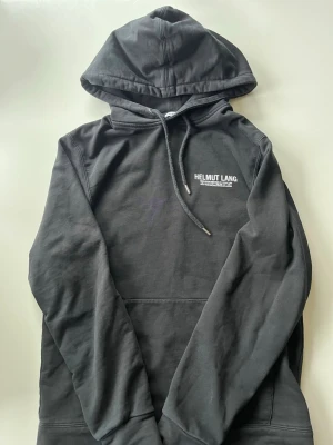 Svart hoodie från Helmut Lang - Snygg svart hoodie från Helmut Lang. Inga defekter förutom möjligtvis lite sprickor i trycket men annars fint skick. 