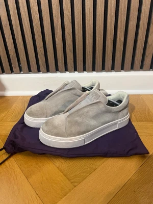 Beige sneakers i mocka från Eytys - Stilrena beige sneakers från Eytys i mjuk mocka med vit tjock sula och lila detalj baktill. Skorna har minimalistisk design utan snörning och en diskret logga på hälen. Perfekta för dig som gillar clean och modern stil.