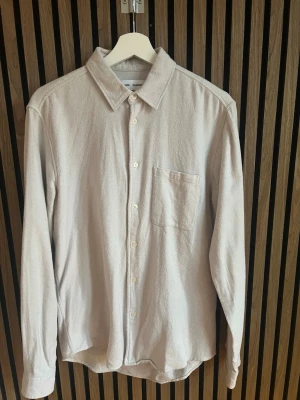 Beige skjorta från Samsøe Samsøe - Stilren beige skjorta från Samsøe Samsøe med klassisk krage och bröstficka. Skjortan har lång ärm och knäppning framtill. Tillverkad i ett mjukt bomullstyg med portugisiskt tyg.