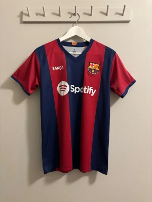 FC Barcelona matchtröja Gavi #6 - Snygg FC Barcelona matchtröja med Gavi och nummer 6 på ryggen. Tröjan har klassiska blå och röda vertikala ränder, klubbmärke på bröstet och sponsorlogga från Spotify. Tillverkad i lätt och ventilerande material, perfekt för fotbollsträning eller match. Sparsamt använd 