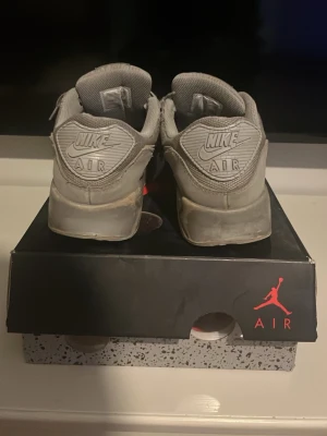 Grå Nike Air Max 90 sneakers - Säljer ett par grå Nike Air Max 90 sneakers med klassisk siluett och synlig Air-enhet i sulan. Skorna har mesh och mockadetaljer, samt Nike-logga på hälen och sidan. Perfekta för dig som gillar streetwear och sportig stil.