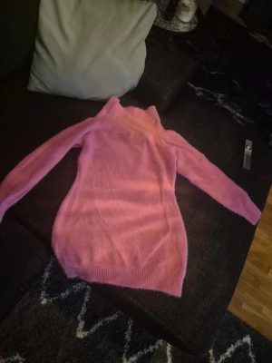 Rosa  stickad klänkng,tröja - Mysig rosa stickad polotröja med lång ärm och ribbade muddar. Tröjan har en hög polokrage och är gjord i ett fluffigt, mjukt material som känns skönt mot huden. Perfekt för dig som gillar färg och vill ha något bekvämt och snyggt.