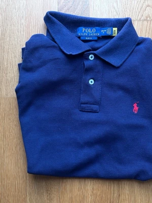 Marinblå pikétröja från Polo Ralph Lauren - Klassisk marinblå pikétröja från Polo 'Ralph Lauren med röd broderad logga på bröstet. Passar dig som är 160. Priset är ej hugget i sten. Kontakta vid minsta fråga!