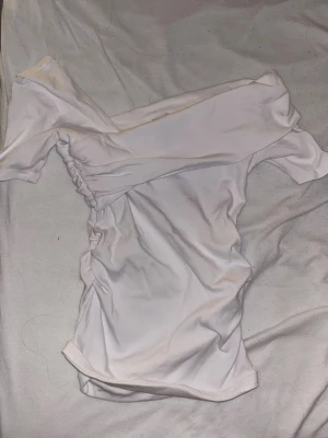 Vit offshoulder topp från Zara - Säljer en snygg vit offshoulder topp från Zara. Toppen har ett coolt snitt med rynkade detaljer på sidan och en asymmetrisk axel. Perfekt för dig som gillar trendiga och stilrena plagg. Materialet är mjukt och stretchigt. I storlek S