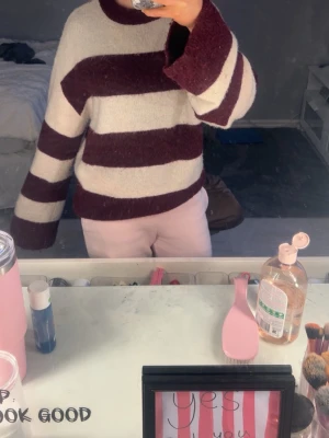 Randig vinröd och vit stickad tröja - Stickad tröja med breda vinröda och vita ränder. Tröjan har en avslappnad passform, rund halsringning och långa ärmar. Materialet är mjukt och mysigt, perfekt för kyligare dagar.