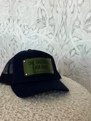 John Hatter keps mörkblå snapback - Mörkblå keps från John Hatter & Co med mesh på sidorna och justerbar snapback. Grön patch framtill med texten “THE TRUTH IS I AM BAD”. Helt ny, säljer eftersom den inte passar min huvudform.