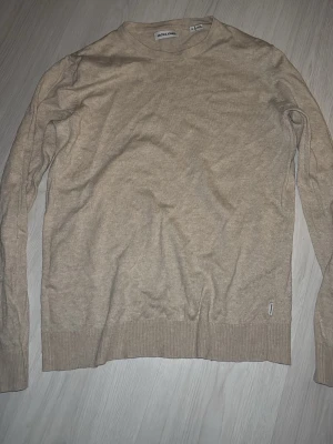 Beige stickad tröja Jack & Jones - Snygg beige stickad tröja från Jack & Jones. Tröjan har rund halsringning, långa ärmar och ribbade muddar vid ärmslut och nederkant. Perfekt för lager på lager och enkel att matcha med olika outfits.