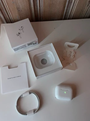 Apple AirPods Pro 2 trådlösa hörlurar - Säljer ett par vita Apple AirPods Pro med laddningsetui och extra silikonpluggar. Hörlurarna är trådlösa och har en stilren, kompakt design i plast. Perfekta för musik, samtal och träning. Originalförpackning och laddningskabel medföljer.