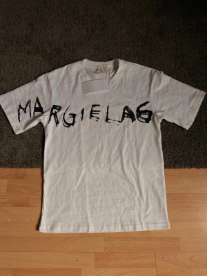 Margiela t-shirt  - Säljer en as fet och sällsynt vit t-shirt från Maison Margiela med svart tryck över bröstet där det står 'MARGIELA6'. Har du fler frågor eller funderingar tveka inte på att höra av dig 🙌
