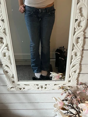 Blå bootcut jeans med fickdetaljer - Säljer ett par blå bootcut jeans med snygga fickdetaljer bak, inklusive dekorativa sömmar och knappar. Jeansen har klassisk femficksdesign och låg midja. Perfekta för dig som gillar en avslappnad men ändå trendig look. Har sytt ned dem, inget man ser när de är på! Pris kan diskuteras!❤️❤️