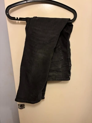 Svarta jeans - Säljer ett par svarta regular/clark jeans med klassisk femficksdesign och diskreta sömmar på bakfickorna. Jeansen har en något tvättad look och är tillverkade i ett mjukt denimtyg som sitter snyggt. Perfekta till en avslappnad streetstyle.