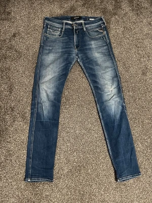 Replay Slim Fit Jeans – W32 L32 - 💥 Säljer mina Replay slim fit-jeans i storlek W32 L32. Snygga blå med riktigt feta slitningar och coola tvättade detaljer – känns som ett riktigt archive-piece! 	•	Klassisk femficksmodell 	•	Vita kontrastsömmar 	•	Läderpatch bak i midjan 	•	Stretchigt denim för skön komfort  Perfekta jeans för dig som vill ha stil med attityd. Säljes för 850 kr.