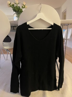 Svart stickad V-ringad tröja - En enkel och stilren svart stickad tröja med V-ringning och långa ärmar. Perfekt basplagg till garderoben och lätt att matcha med olika outfits. Tröjan har en mjuk och lite luddig yta som ger en mysig känsla. Tröjan är ganska nopprig.