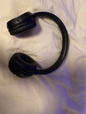 Svarta over-ear hörlurar från JBL - Säljer ett par svarta over-ear hörlurar från JBL. De har en stilren design med vadderade öronkuddar i konstläder och justerbart huvudband. Perfekta för att lyssna på musik eller poddar med bra ljudkvalitet.