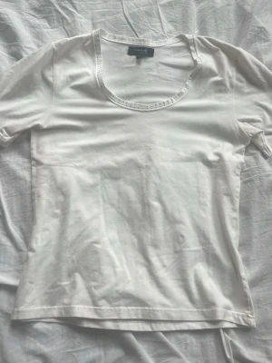 Vit topp från Claire.dk med rund hals - Säljer en enkel och stilren vit topp från Claire.dk med rund halsringning och korta ärmar. Toppens material är mjuk bomull och den har en diskret dekor runt halsen. Perfekt för att matcha med jeans eller kjol.