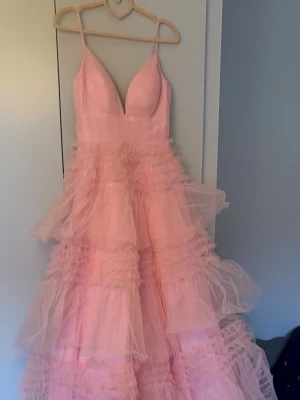 Rosa glittrig långklänning med volanger - Drömmig rosa långklänning med tunna axelband, djup v-ringning och flera lager av volanger i glittrigt tyllmaterial. Skulle haft som bal klänning i 9an men den kom tyvärr för sent, därav helt orörd och oanvänd💕💕Klänning ser ut som den gula på sista bilden fast rosa 