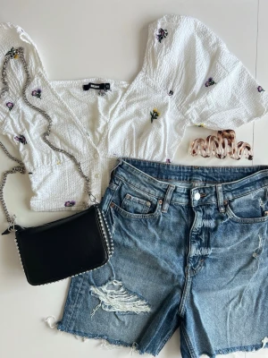 Cute outfit bundle: blommig topp + denim shorts + väska med studs + hårklämma - stl xs/s - Trendig outfit bundle 🌸  Kit med 4 delar: • Vit/blommig croppad topp med knappar & puffärm • mörkblå jeansshorts (stl s) • svart väska med studs runtom • vågig hårklämma. Varumärken: Bikbok, H&M.  Perfekt somrig & gullig outfit 💖 Alla plagg i fint skick. Kolla gärna in mina andra kit 💌 Fler bilder finns!