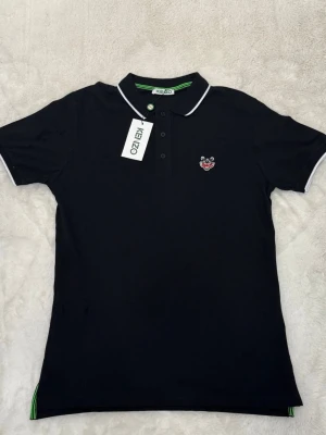 Svart pikétröja från Kenzo - Snygg svart pikétröja från Kenzo med vit kant på krage och ärmslut. 