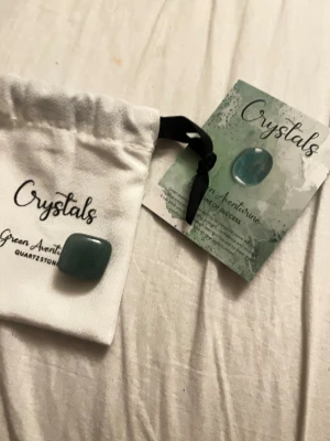 Grön aventurin kristallsten - Säljer en grön aventurin kristallsten från Crystals, levereras med en vit tygpåse och informationskort. Stenen är slät, rektangulär och har en djup grön färg. Perfekt som accessoar eller för dig som gillar kristaller och stenar.