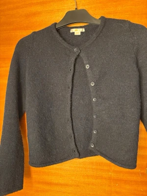 Gina tricot   - Klassisk mörkblå kofta i mjuk ull med rund halsringning och knäppning framtill med svarta knappar. Långärmad och rak passform, perfekt att slänga över en t-shirt eller topp. Enkel och stilren design som funkar till det mesta.