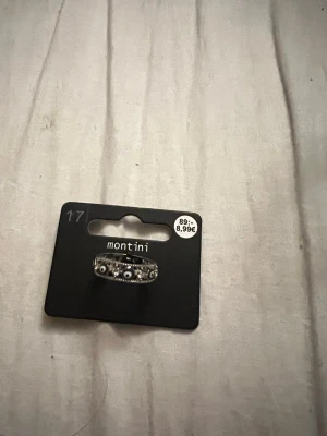 Silverfärgad ring med pärldetaljer - Stilren silverfärgad ring från Montini med små vita pärlor och gnistrande stenar runt hela ringen. Ringen har en klassisk, rund form och passar perfekt för dig som gillar detaljerade accessoarer.