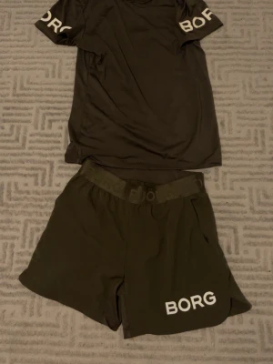 Svart träningsset från Björn Borg - Snyggt svart träningsset från Björn Borg med t-shirt och shorts. T-shirten har vita BORG-tryck på båda ärmarna och shortsen har samma tryck på ena benet. Materialet är lätt och andas, perfekt för gym eller löpning.